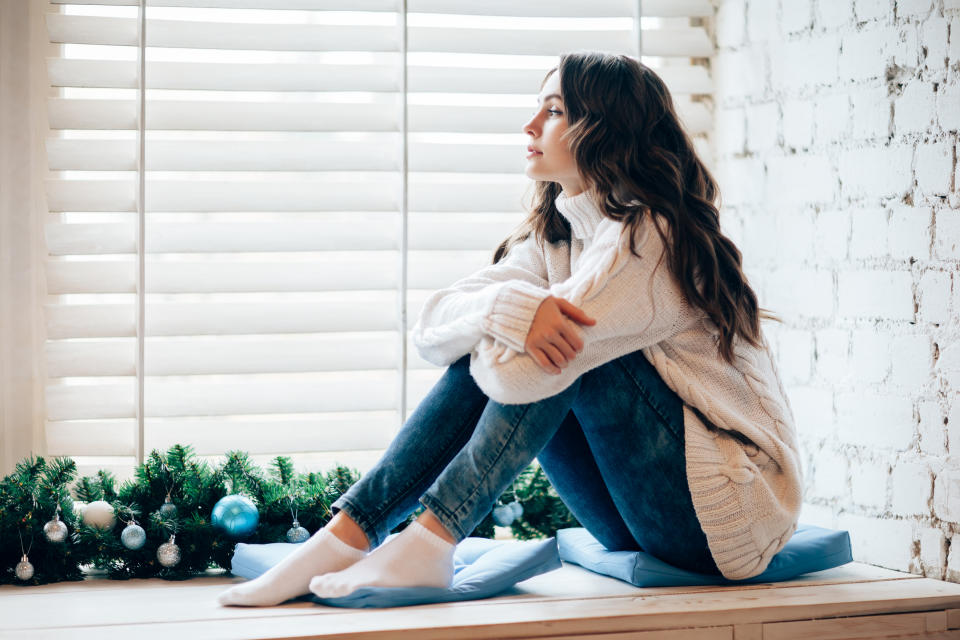 Young beautiful woman relaxing on window sill in christmas decorated home. Holiday concept