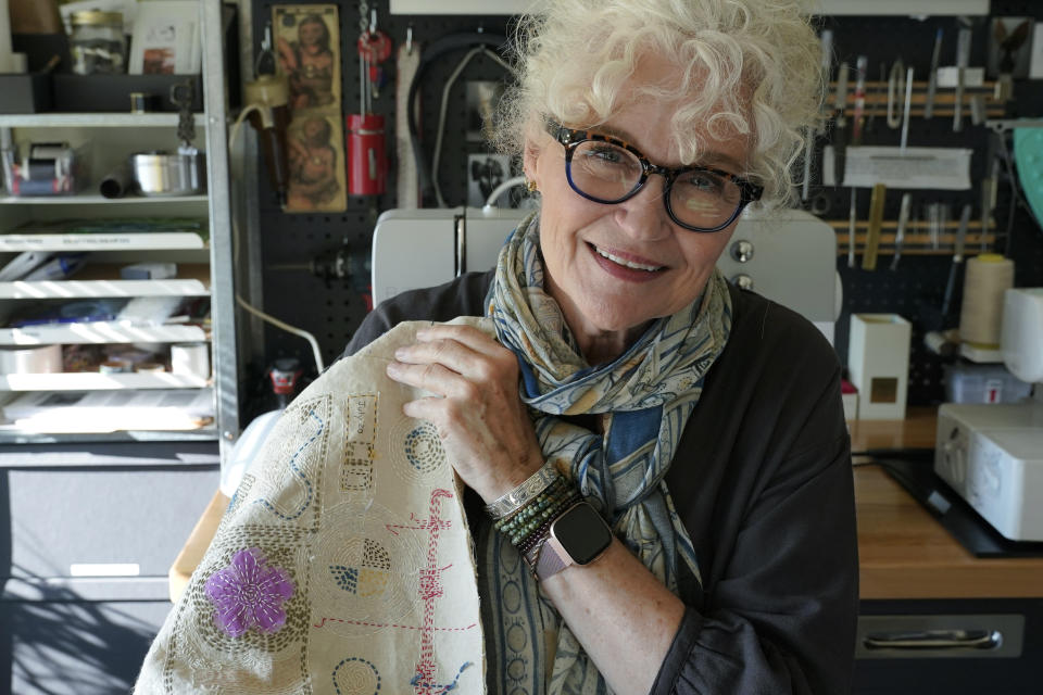 Mary Beth Orr holds an embroidery panel from her "stitch journal" as she poses for a photo in her home, Tuesday, Aug. 23, 2022 in Burien, Wash., south of Seattle. Orr used to have five or six drinks every evening and more on weekends before she enrolled in a study in 2018 to see if the compound in psychedelic mushrooms could help heavy drinkers cut back or quit entirely. She stopped drinking entirely for two years, and now has an occasional glass of wine, and credits psilocybin for her progress. (AP Photo/Ted S. Warren)