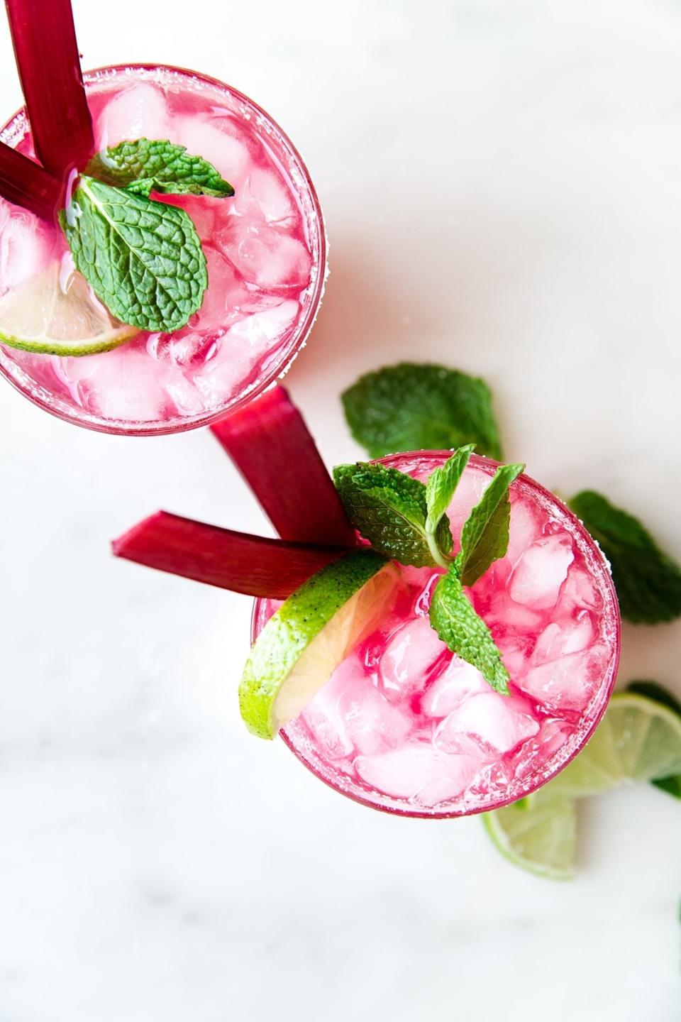 Two glasses of iced rhubarb cocktails garnished with lime and mint