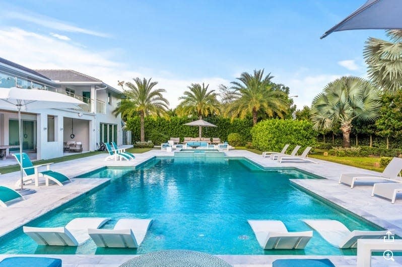 picture of pool with four beach chairs in front of it and palm trees in the background