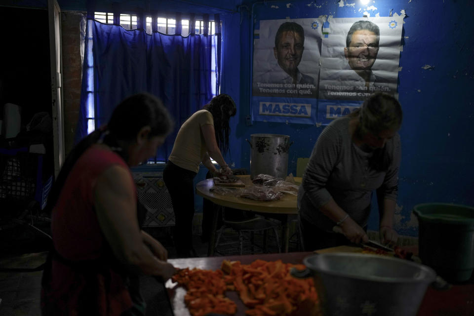 Mónica Figueroa, Norma Cabral y Alicia, preparan comida mientras en el fondo una pared se encuentra adornada por pancartas de campaña del ministro de Economía Sergio Massa, el candidato oficialista, en un comedor gestionado por el Movimiento Evita, una organización social peronista, en Ciudad Evita, a las afueras de Buenos Aires, el lunes 13 de noviembre de 2023. (AP Foto/Natacha Pisarenko)