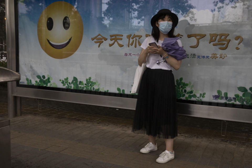 A woman wearing a mask to curb the spread of the new coronavirus waits near a billboard with a smiley face and the slogan "Have you smiled today?" on the streets of Beijing, Saturday, May 30, 2020. (AP Photo/Ng Han Guan)