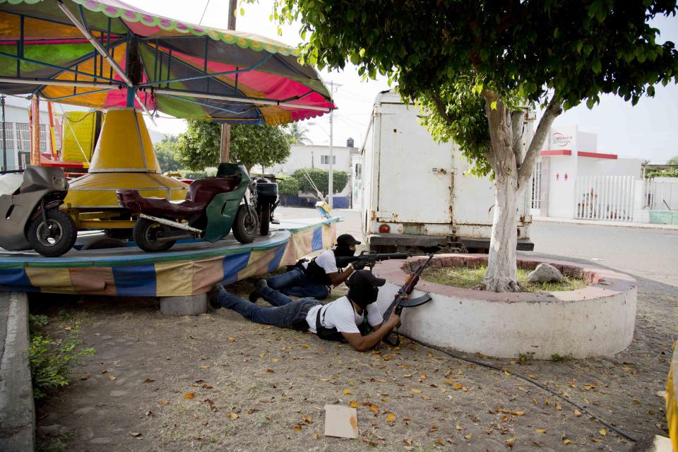 Integrantes del Consejo de Autodefensa de Michoacán (CAM) se resguardan durante una balacera contra presuntos integrantes del cártel de los Caballeros Templarios en el pueblo de Nueva Italia, México, el domingo 12 de enero de 2014. Cientos de miembros de civiles armados llamados autodefensas redoblaron su ofensiva contra los narcotraficantes en el estado de Michoacán, en el occidente del país. (Foto AP/Eduardo Verdugo)