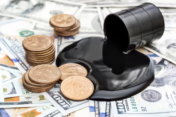 A miniature barrel of oil spilling on a pile of dollars and coins.