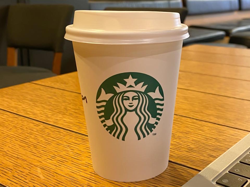 Starbucks coffee cup on a wooden table next to an open laptop