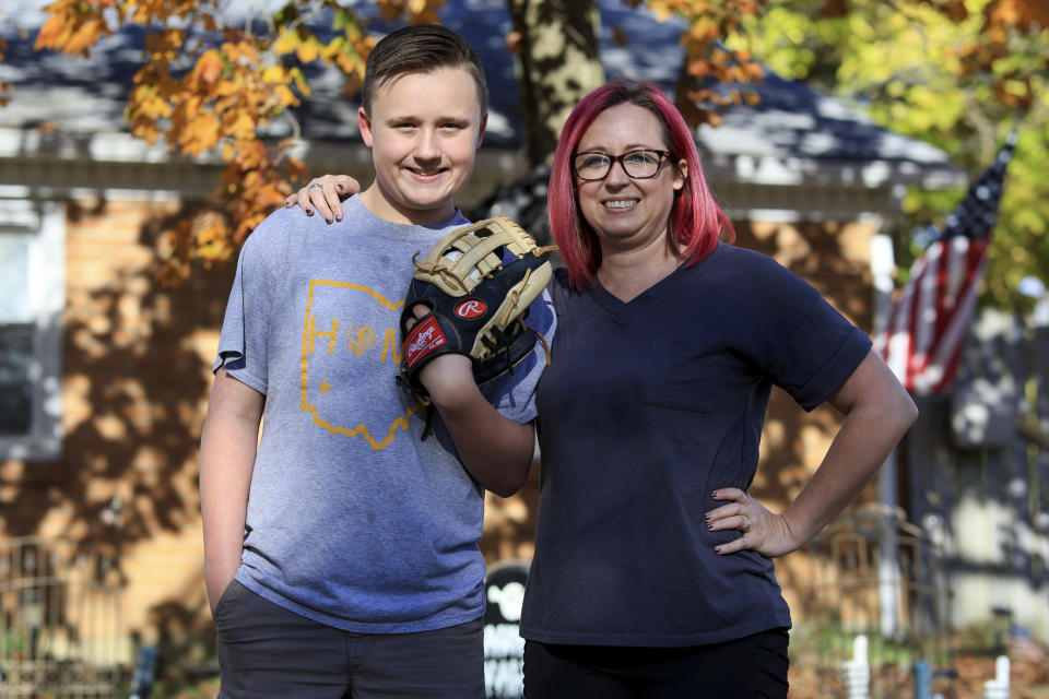 Liam, left, and his mother, Rachel Kennedy, pose for a photo as they stand in their front yard Friday, Oct. 28, 2022, in Monroe, Ohio. Sticker shock in youth sports is nothing new, but the onslaught of double-digit inflation across America this year has added a costly wrinkle on the path to the ballparks, swimming pools and dance studios across America. It has forced some families, like Kennedy's, to scale back the number of seasons, or leagues, or sports that their kids can play in any given year. (AP Photo/Aaron Doster)