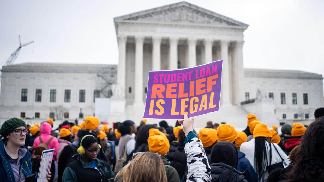 A crowd of supporters stands in front of the Supreme Court. One person holds a sign reading: Student loan relief is legal.