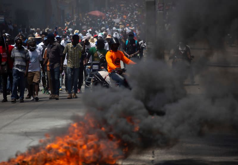 Demonstrators march near a burning road block during a protest against the government of President Jovenel Moise, in Port-au-Prince