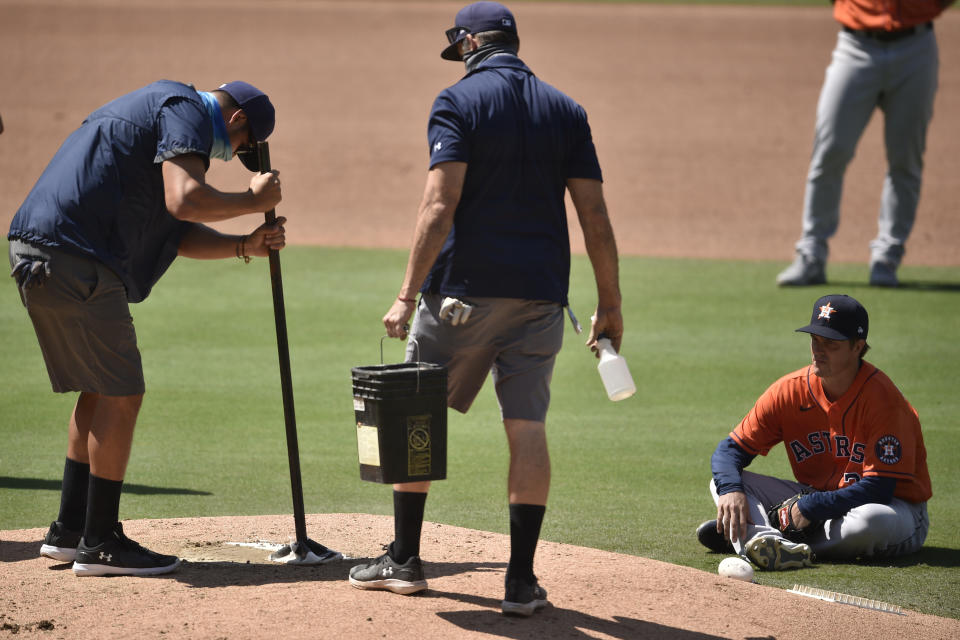 Houston Astros starting pitcher Zack Greinke, right, sits on the field as the San Diego Padres grounds crew work on the pitching mound during an in-game delay during the fourth inning of a baseball game in San Diego, Sunday, Aug. 23, 2020. (AP Photo/Kelvin Kuo)