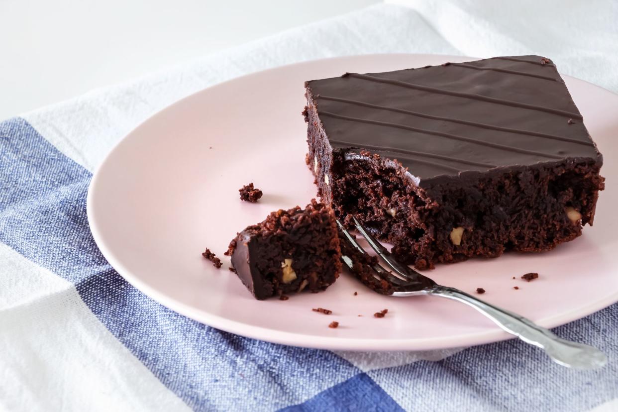 Chocolate vegan brownie cake with nuts. Pink plate. Light background.