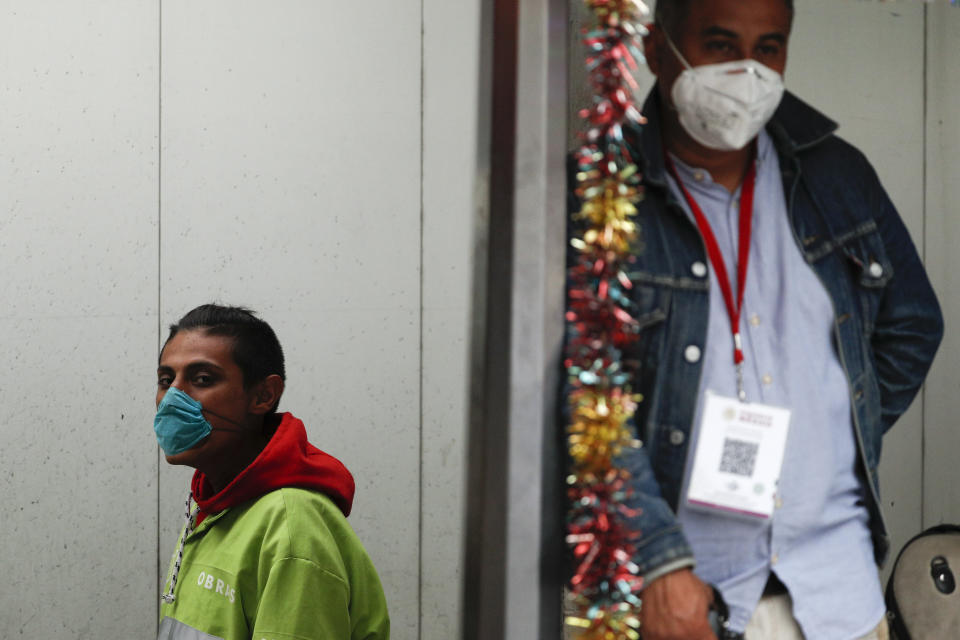 A city cleaner, left, and a journalis, both wearing protective face masks, stand outside an event where Mexican President Andres Manuel Lopez Obrador was visiting a hospital that will be converted to receive patients suffering from Covid-19, in the Coyoacan district of Mexico City, Friday, April 3, 2020. Lopez Obrador said Thursday that sections of designated public hospitals were being isolated and prepared with an average of eight beds and respirators to care for an expected influx of patients with the new coronavirus. (AP Photo/Rebecca Blackwell)