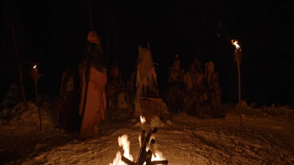 Teenage girls dressed in beast hide sitting around a bonfire