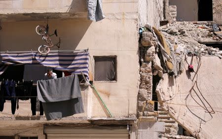 A man looks out from a balcony next to a collapsed building in Aleppo's Kalasa district, Syria April 11, 2019. REUTERS/Omar Sanadiki