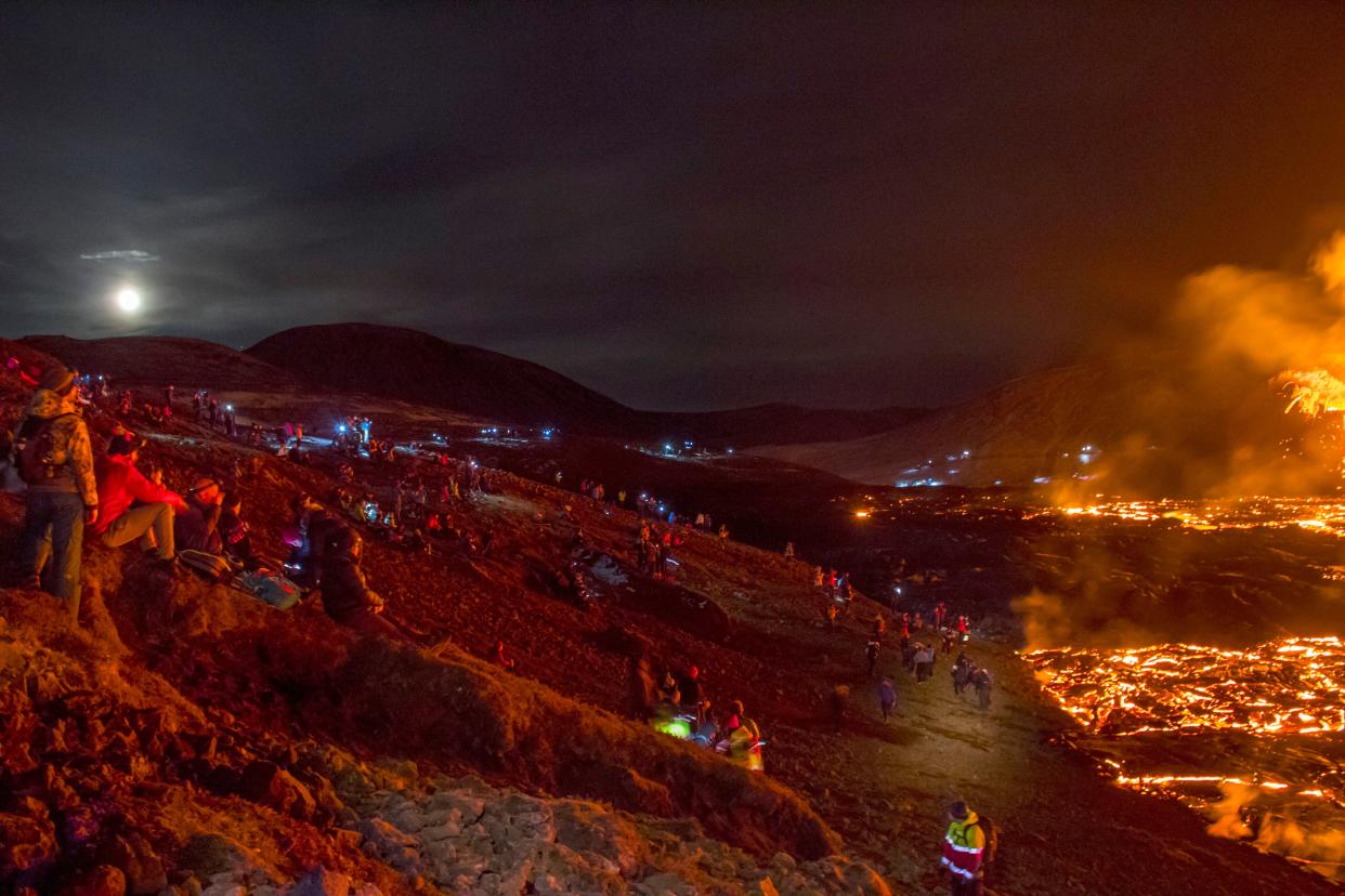 People watch as lava flows from an eruption of a volcano on the Reykjanes Peninsula in southwestern Iceland late on Monday, March 29, 2021. Iceland's latest volcano eruption is still attracting crowds of people hoping to get close to the gentle lava flows. The eruption in Geldingadalur, near Iceland's capital Reykjavik, is not seen as a threat to nearby towns and the slow flows mean people can get close to action without too much harm.