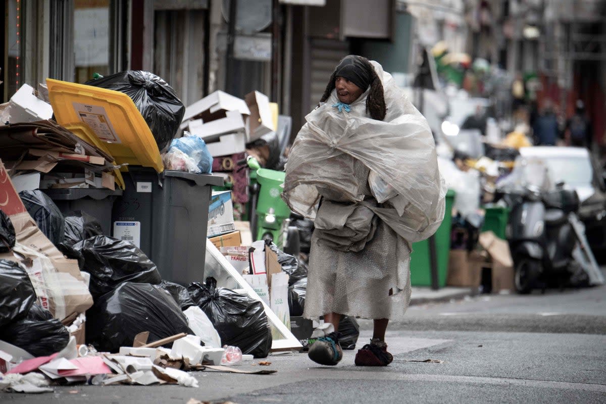 A homeless man, covered with plastic bags, walks past garbage bags that have been piling up on the pavement as waste collectors are on strike (AFP via Getty Images)