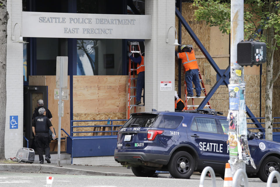 Workers put up plywood over the windows of a Seattle police precinct Monday, June 8, 2020, in Seattle, where protests continued the night before over the death of George Floyd, a black man who was in police custody in Minneapolis. Just days after Seattle's mayor and police chief promised a month-long moratorium on using a type of tear gas to disperse protesters, the department used it again. (AP Photo/Elaine Thompson)