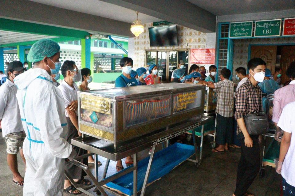 People wearing face masks wait while caskets with bodies are queued outside a crematorium at the Yay Way cemetery in Yangon, Myanmar, Wednesday July 14, 2021. The number of people dying in Myanmar's biggest city, Yangon, which is facing a coronavirus surge and a shortage of oxygen to treat patients, has been climbing so quickly that charity groups said Wednesday they are almost overwhelmed. (AP Photo)