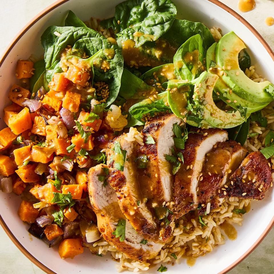 sliced chicken in a grain bowl with sweet potatoes, avocados, spinach and a peanut dressing