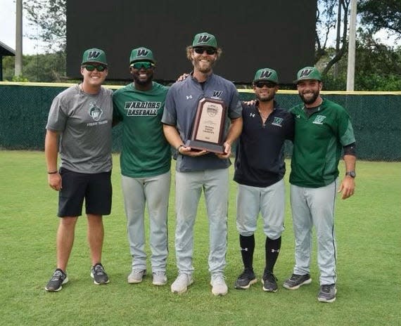 Webber International head baseball coach Collin Martin, pictured in the middle, holds the opening-round trophy surrounded by some of his players.