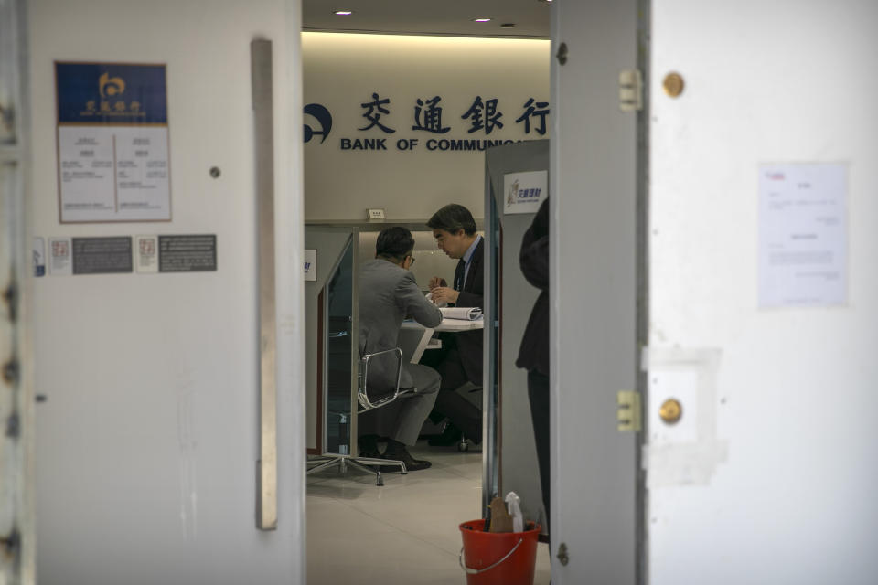 A bank employee talks with a customer as seen through barriers built around the entrance of a Bank of Communications branch in Hong Kong, Friday, Oct. 25, 2019. Banks, retailers, restaurants and travel agents in Hong Kong with ties to mainland China or perceived pro-Beijing ownership have fortified their facades over apparent concern about further damage after protesters trashed numerous businesses following a recent pro-democracy rally. (AP Photo/Mark Schiefelbein)