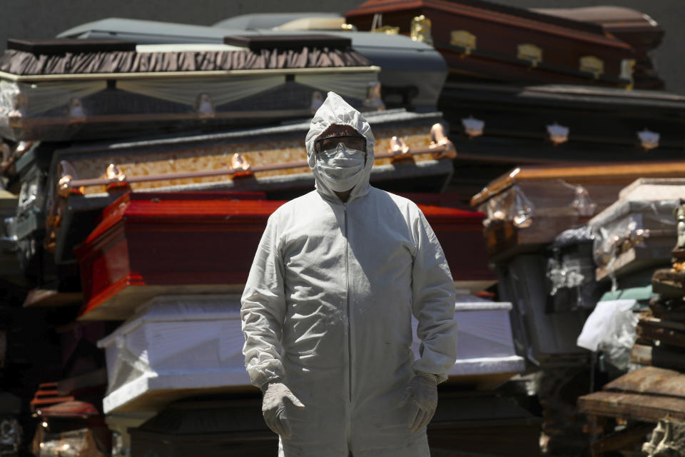 An employee of Xochimilco's crematorium waits for a corpse, suspected to have died of the new coronavirus, in Mexico City, Monday, May 4, 2020. He is standing next to pile of discarded coffins that contained people who died of COVID-19 disease, and are waiting to be destroyed at the site. (AP Photo/Fernando Llano)
