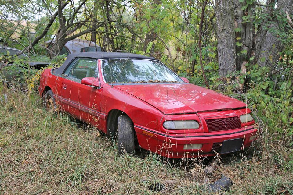 <p>Here’s one of the more youthful and colorful residents of Ron’s Auto Salvage. It’s a facelifted third generation Chrysler LeBaron convertible, which dates it to between 1993 and 1995. These cars are easily identified by their <strong>flush headlamps</strong>, which replaced the retractable hidden lights of the earlier cars.</p>