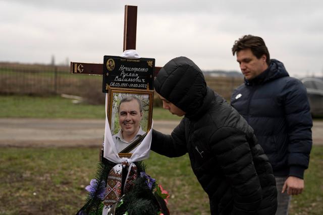 Yura Nechyporenko, 15, kisses the pictures of his father Ruslan Nechyporenko in front of his uncle Andriy Nechyporenko, at the cemetery in Bucha, on the outskirts of Kyiv, Ukraine, on Thursday, April 21, 2022. The teen survived an attempted killing by Russian soldiers while his father was killed, and now his family seeks justice.