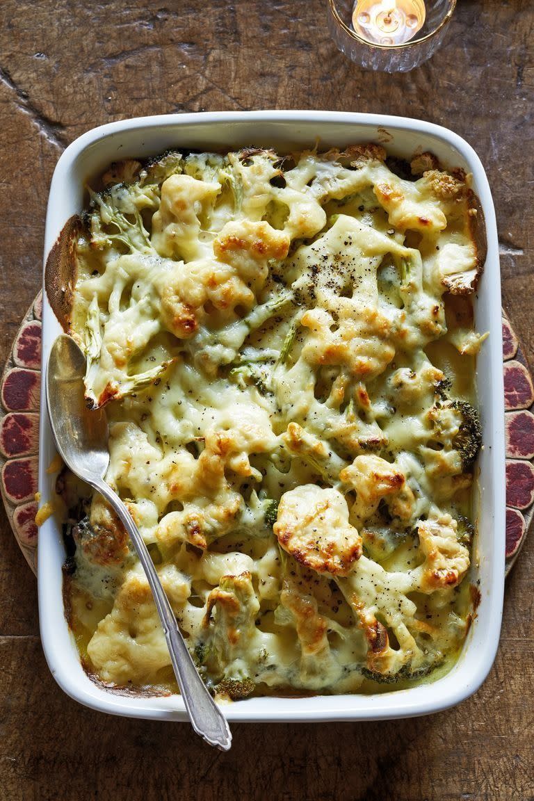 broccoli and cauliflower gratin in a white baking dish with a spoon for serving