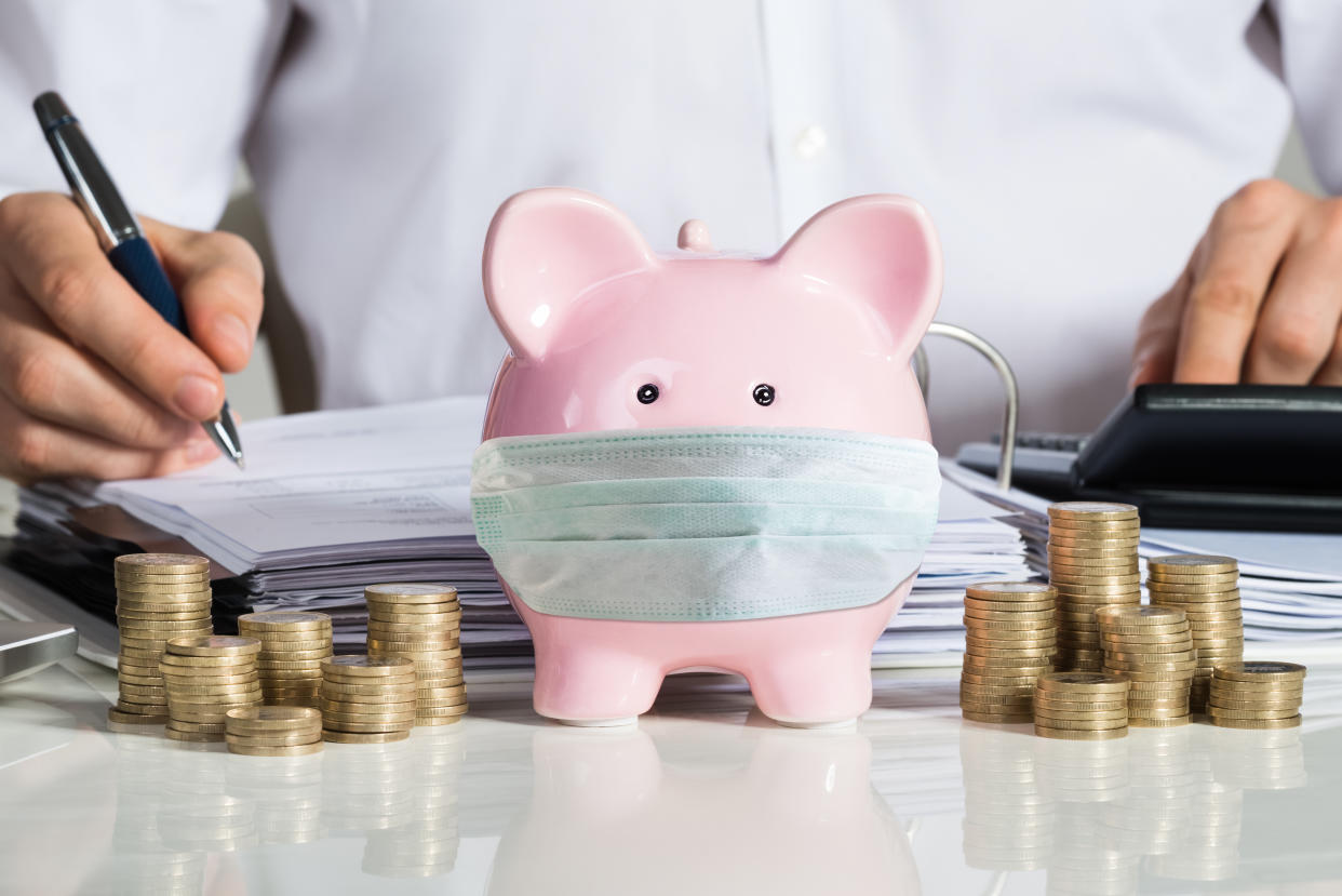 Midsection of businessman calculating invoice with piggybank and coins at office desk