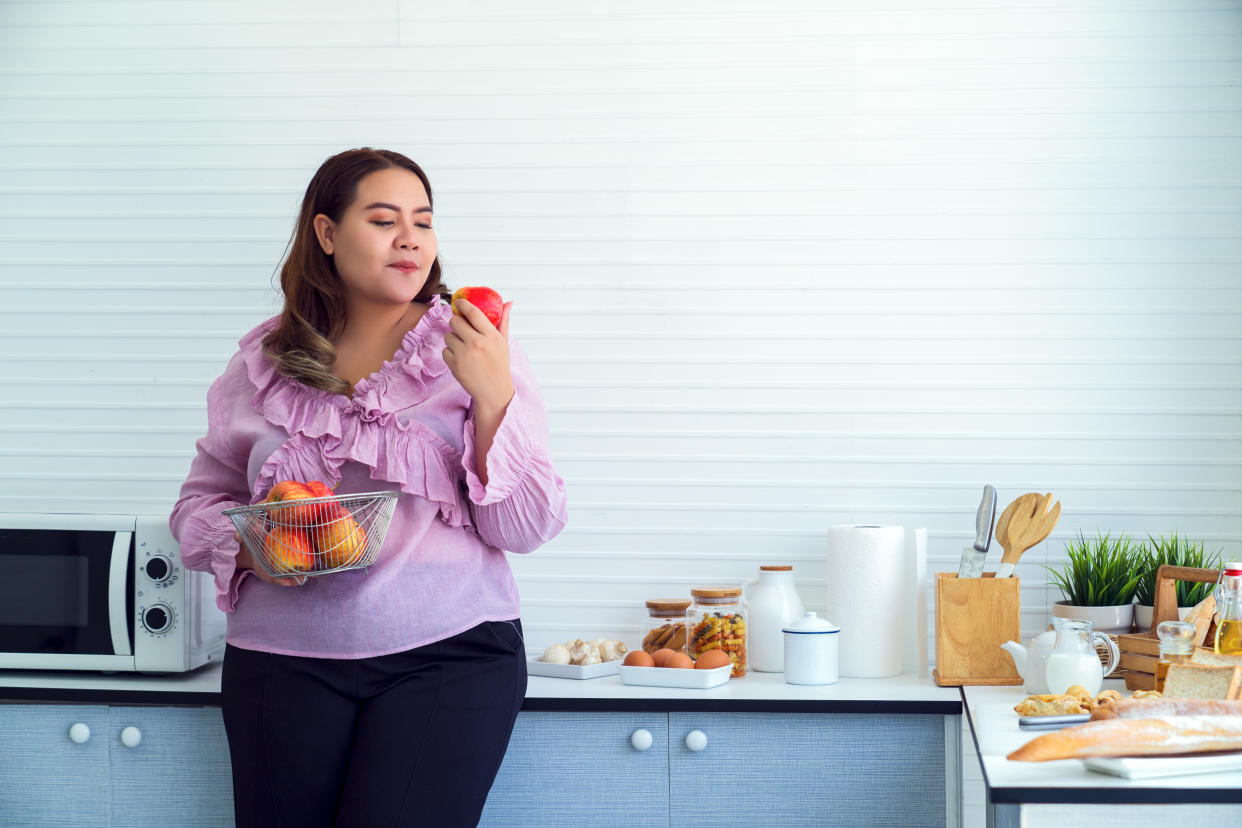 Shot of overweight woman eating an apple in her kitchen at home for weightloss.