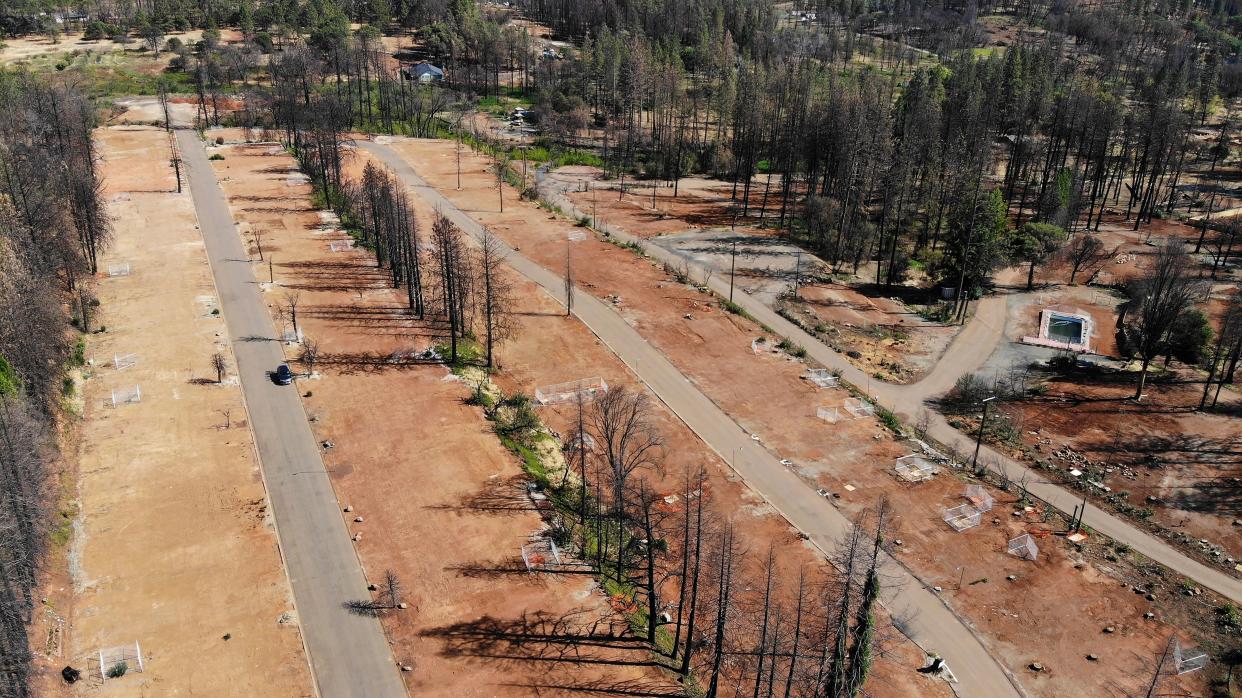 Aerial view of the flattened remains of a mobile home park, which includes roads that encircle dirt patches with the foundations of former homes visible.