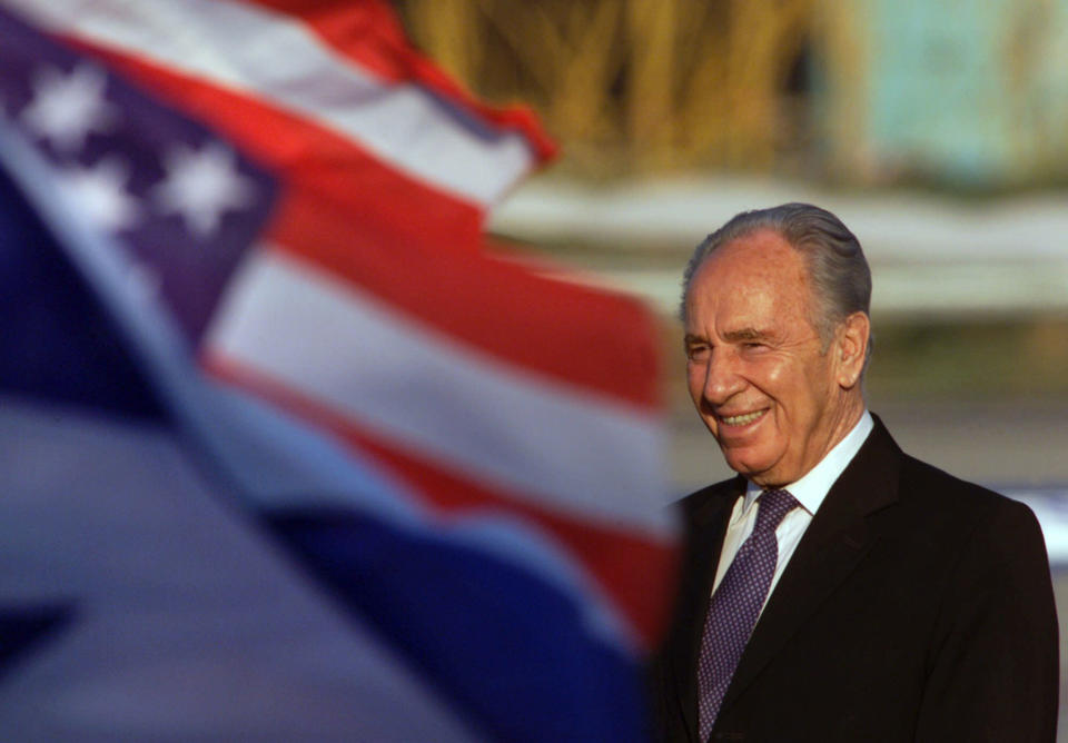 <p>Israeli Foreign Minister Shimon Peres, behind an Israeli, left, and a U.S. flag, center, waits for U.S. Secretary of State Colin Powell shortly before his arrival at Ben Gurion International airport near Tel Aviv, Israel Wednesday, June 27, 2001. (AP Photo/Lefteris Pitarakis) </p>