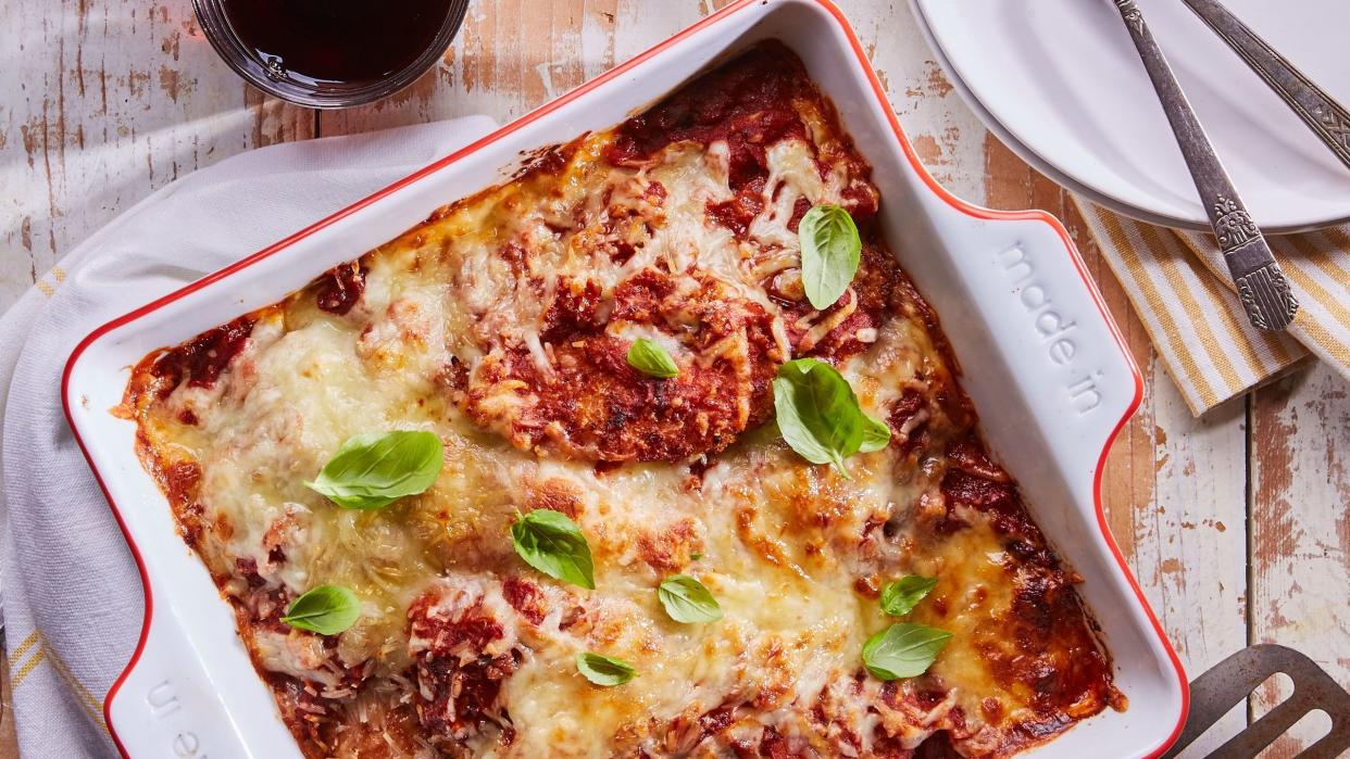 crispy chicken parmesan baked in a white square baking dish with melted cheese and fresh basil leaves on top