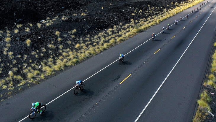 Several cyclists pass a black rock volcanic area