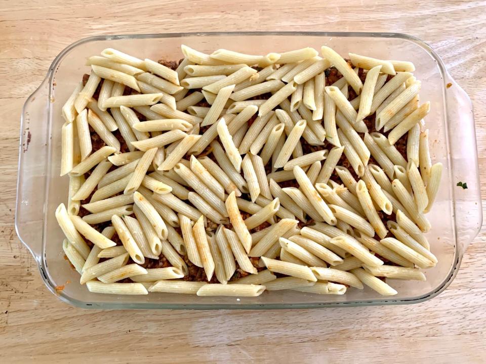 Cooked pasta on top of meat mixture in glass baking dish