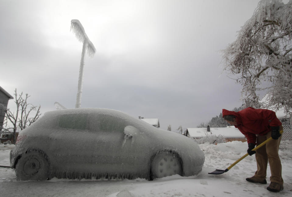 A man shovels ice next to ice-covered car in Postojna