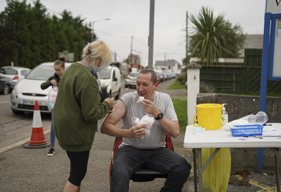 <p>SUMMERCOURT,  UNITED KINGDOM - SEPTEMBER 25: A member of the public eats candy floss from the nearby fairground while he receives a Pfizer Covid vaccination at an NHS walk-up vaccination unit outside the village hall on September 25, 2021 in the village of Summercourt, near Newquay, Cornwall, United Kingdom. Additional Covid-19 support measures introduced with government backing to tackle the rising infection during the summer are expected to end for Cornwall on October 1st. Support has included leaflet drops, extra vaccine clinics and engaging with young people. (Photo by Hugh Hastings/Getty Images)</p>
