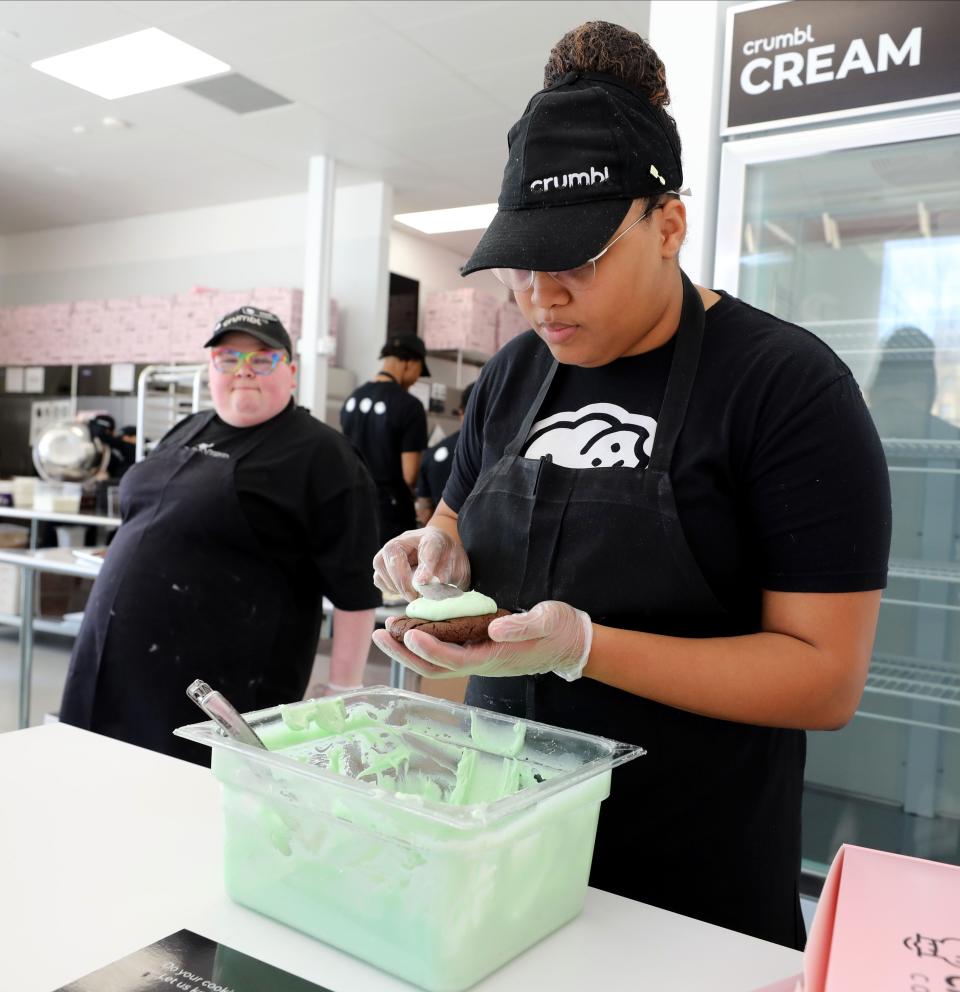 Gabrielle Salaam, the general manager at Crumbl Cookies on North Central Avenue in Hartsdale, decorates a Mint Brownie cookie, photographed March 15, 2023. Looking on is Madi Lee, a baker at the shop. 