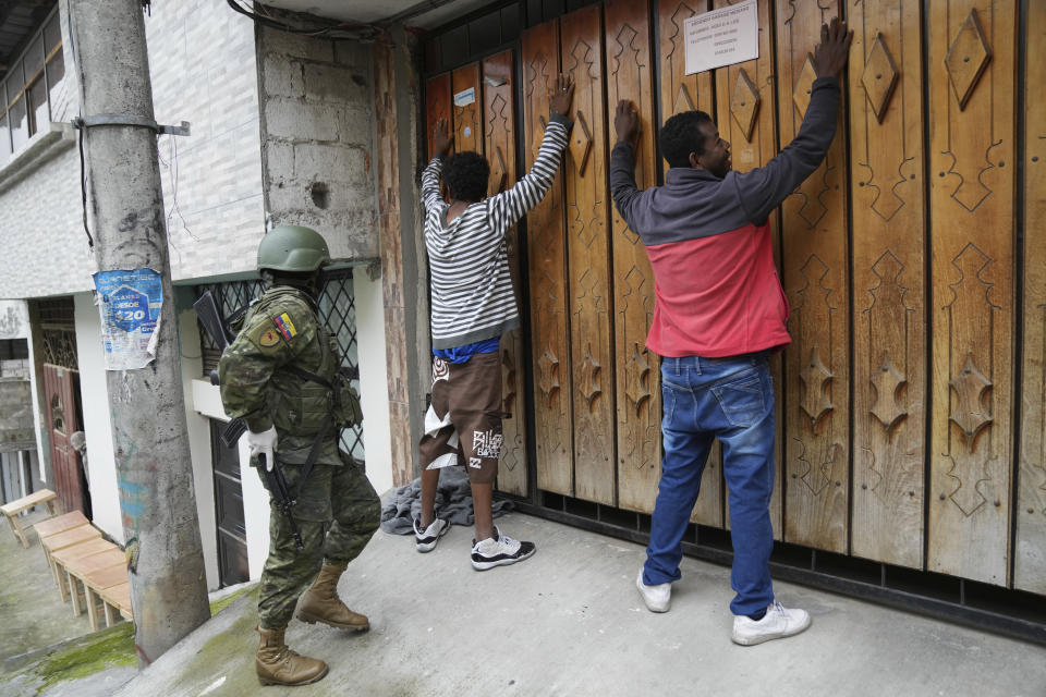 Dos personas contra una puerta con las manos en alto y un militar procede a registrarlos mientras patrullan por el sur de Quito, Ecuador, el viernes 12 de enero de 2024, como secuela a la fuga de dos cabecillas de bandas criminales de prisión. El presidente Daniel Noboa decretó el lunes el estado de emergencia nacional debido a una ola de criminalidad, una medida que permite a las autoridades suspender los derechos de las personas y movilizar a los militares. El gobierno también impuso un toque de queda. (Foto AP/Dolores Ochoa)