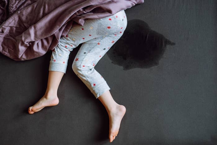 A child in pajama pants covered with stars lies in bed next to a wet spot on the mattress