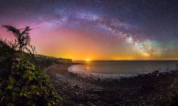 ISLE OF WHITE, GREAT BRITAIN - MAY 13: A view of the Milky Way taken by Chad Powell on a DSLR camera on May13, 2015. Taken at Mount Bay, St Lawrence just minutes before the moon crept above the horizon and washed out the sky. The bright light prominent in the very centre of the image, often mistaken as the sun in my images is a large container ship, often anchored in the distance, ready to dock at Portsmouth/Southampton harbour.   LIGHTS from the Milky Way dazzle above the Isle of White in these rarely seen British sky-scapes. Chad Powell captured images of spectacular light patterns above the familiar beach scenes of England?s largest island. The 23-year-old used a DSLR camera to enhance the Milky Way from the white strip visible to the naked eye into an explosion of colourful lights. The graphic designer from Ventnor, Isle of Wight, used the local architecture, coves and plant life of the island in the foreground of his photographs to create a contrast with the dramatic sky. Wheat fields, night daisies and a medieval lighthouse are some of the scenes Chad captures against the startling natural light displays.  PHOTOGRAPH BY Chad Powell / Barcroft Media  UK Office, London. T +44 845 370 2233 W www.barcroftmedia.com  USA Office, New York City. T +1 212 796 2458 W www.barcroftusa.com  Indian Office, Delhi. T +91 11 4053 2429 W www.barcroftindia.com