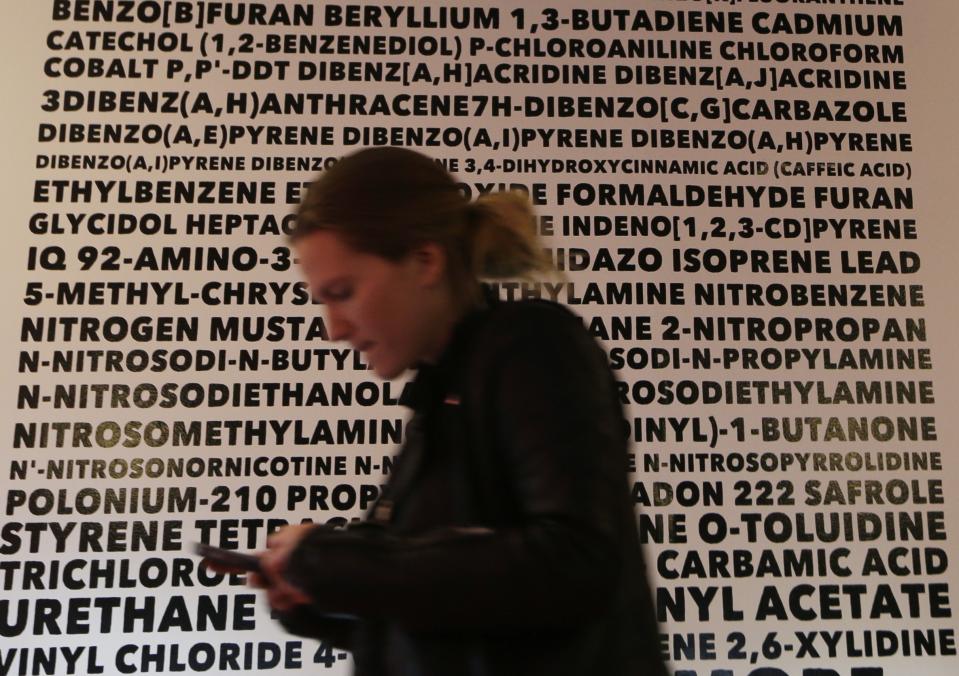 In this Feb. 20, 2014 photo, Talia Eisenberg passes a white “wall of doom,” at the Henley Vaporium in New York. The wall lists in big black letters the numerous tars and chemicals found in tobacco cigarettes, but absent in e-cig use if one is careful about the liquids purchased. (AP Photo/Frank Franklin II)