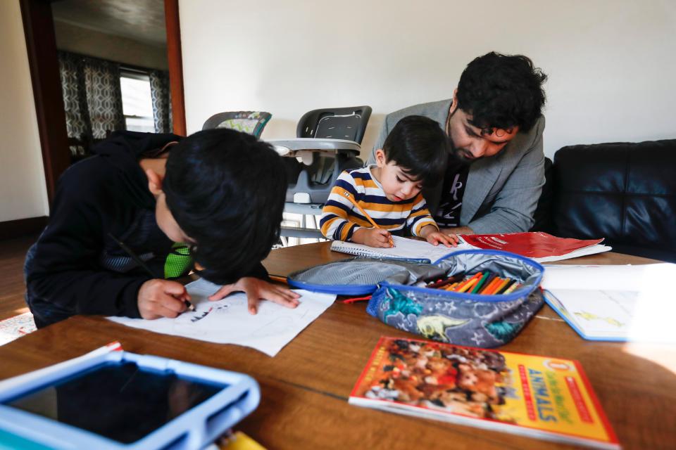 Romal Noori helps his 2-year-old son Mohammad Sodais write English letters as 6-year-old Abdul Bais colors at their home on Saturday, Dec. 17, 2022.