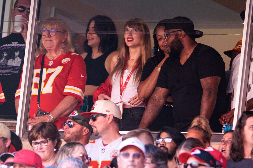 Taylor Swift stands among a crowd of people, many of whom wear Kansas City Chiefs gear.