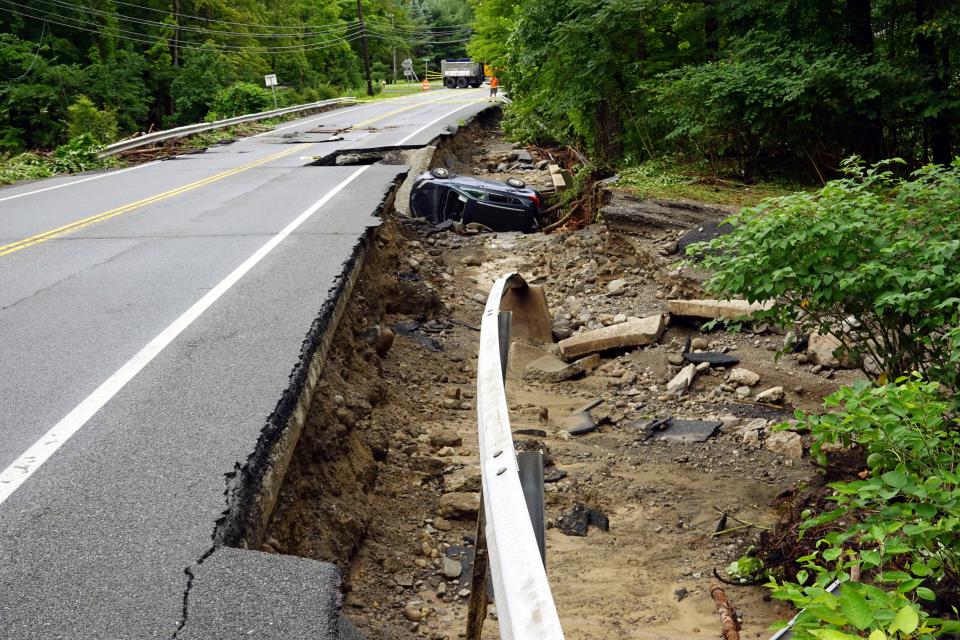 A damaged car lays off a collapsed roadway along Route 32 in the Hudson Valley near Cornwall, N.Y., Monday, July 10, 2023. Heavy rain has washed out roads and forced evacuations in the Northeast as more downpours were forecast throughout the day. (AP Photo/Paul Kazdan)