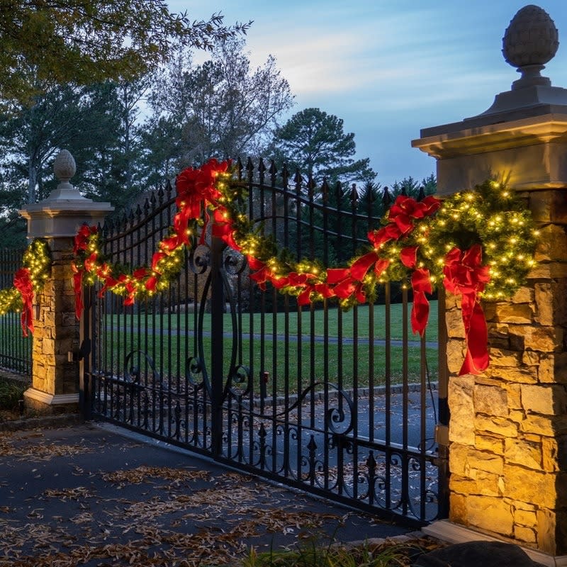 an outdoor garland on a gate with the bows attached to it