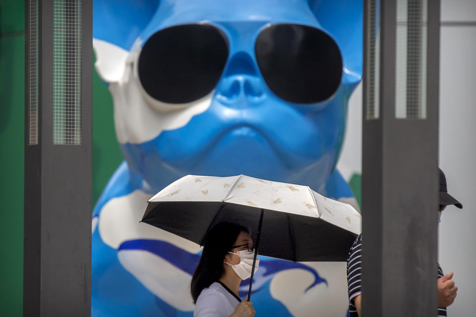 A woman wearing a face mask to protect against the new coronavirus walks past a statue at an outdoor shopping mall in Beijing, Saturday, July 4, 2020. China reported a single new case of coronavirus in Beijing on Saturday, plus a few more cases elsewhere believed to have come from abroad. (AP Photo/Mark Schiefelbein)