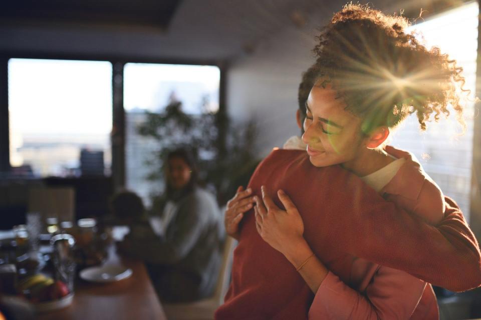 teenage girl with eyes closed embracing her brother in dining room at home