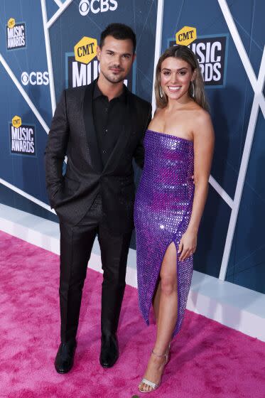 A man all in black and a woman in a sparkly strapless dress pose together on a red carpet at an awards show