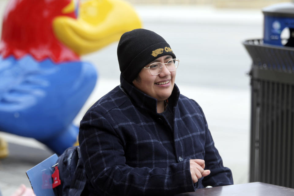 University of Kansas junior Raine Flores-Peña talks to fellow students outside the university's Memorial Union with a statue of the college's Jayhawk mascot in the background, Tuesday, March 26, 2024, in Lawrence, Kan. Flores-Peña is transgender and an LGBTQ+ rights activist who works at the university's Center for Sexuality and Gender Diversity. (AP Photo/John Hanna)